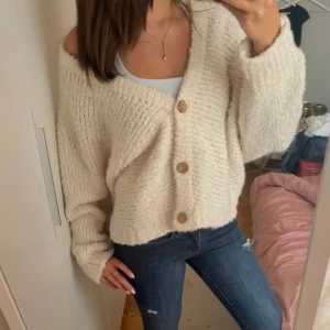 Beige stickad kofta från Garconne - Supermjuk och oversized beige stickad kofta från Garconne med stora träknappar framtill. Koftan har lång ärm, v-ringad hals och en loose fit som ger en chill vibe. Perfekt att slänga över ett linne eller t-shirt för en avslappnad look.