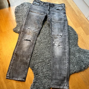 jeans Jack & Jones jjglenn jjblair  - Säljer ett par grå jeans från Jack & Jones med slitna detaljer och trasiga partier på benen. Jeansen har klassisk femficksdesign, raka ben och tydliga slitningar både fram och bak. Materialet är denim och färgen är tvättad grå med ljusare partier.