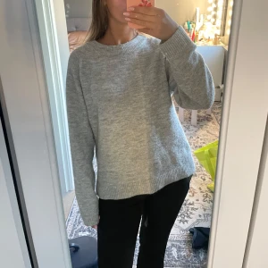 Grå stickad tröja med rund hals - Enkel och stilren grå stickad tröja med rund halsringning och långa ärmar. Tröjan har en relaxed passform och ribbade muddar vid ärmslut och nederkant. Perfekt för lager-på-lager under kyliga dagar.