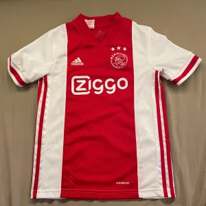 Ajax Amsterdam röd-vit fotbollströja - Ajax Amsterdam matchtröja från Adidas med klassisk röd mittpanel och vita sidor. Använt den några gånger men den är helt ren och i bra skick. Storlek 152, pojkar och pris kan diskuteras. Skickar inom 1-3 dagar