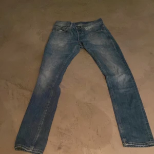 Blå jeans från Dondup, Made in Italy - Säljer ett par snygga blå jeans från Dondup, Made in Italy. Jeansen har klassisk femficksdesign, raka ben och coola detaljer som broderad siffra och spänne på bakfickan. Perfekta för dig som gillar italiensk streetstyle. Skinny fit men lite sönder vid fickan 