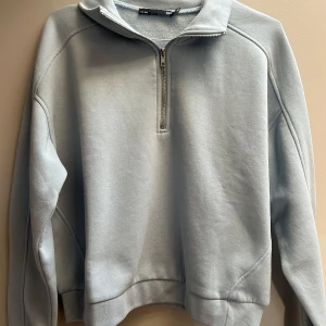 Ljusblå half zip hoodie från H&M - Snygg ljusblå hoodie från H&M med half zip-dragkedja och hög krage. Tröjan har en relaxed passform och är tillverkad i mjuk bomullsmix. Perfekt för chill dagar eller när du vill ha en clean och enkel look.