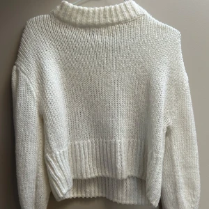 Vit stickad tröja med polokrage - Mysig vit stickad tröja med polokrage och långa ärmar. Tröjan har en chunky ribbstickad kant vid halsen, ärmsluten och nederkanten. Perfekt för lager-på-lager och ger en clean och stilren look.