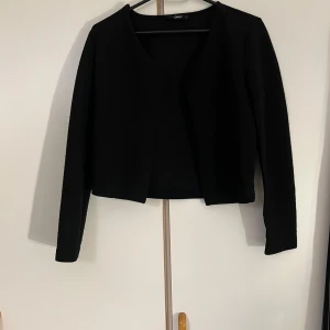 Svart cardigan jacka från ONLY - Svart ribbad cardigan jacka från ONLY i storlek S. Jackan har lång ärm, öppen framtill och är tillverkad i ett stretchigt, ribbat material som ger en snygg och stilren look. Perfekt att slänga över en topp för en clean outfit.