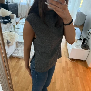 Grå stickad polotopp från BikBok - Mysig grå stickad polotopp från BikBok i storlek S. Toppen är ärmlös med hög krage och har slitsar i sidorna. Inga defekter 