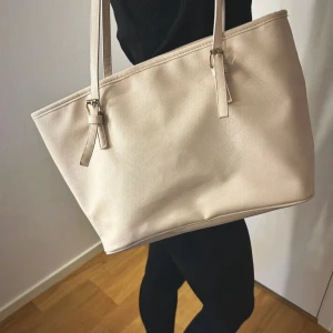 Beige axelväska med innerfack - Stilren beige axelväska med raka linjer och långa remmar. Banden är är lite sönder derutav priset men går att limma eller sy för den som vill. Finns en magnet i som man kan stänga ihop väskan. Köpt på Lindex för runt 200kr. 