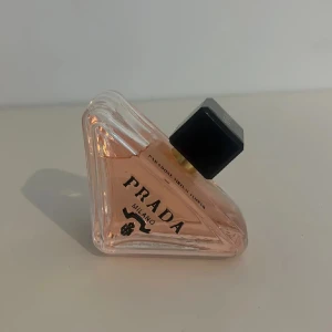 Prada Paradoxe Eau de Parfum 90ml - Prada Paradoxe Eau de Parfum i en unik trekantig glasflaska med ljusrosa doftvätska och svart fyrkantigt lock. Flaskan rymmer 90 ml och har tydlig Prada Milano-logga framtill. En lyxig och modern parfym som sticker ut i samlingen.