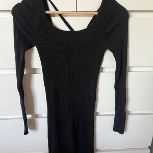 Svart ribbad långklänning Vero Moda - Säljer en svart långklänning från Vero Moda i ribbad bomull. Klänningen har långärmade smala ärmar, rundad halsringning och snygga korsade band i ryggen. Passformen är tight och materialet är mjukt och stretchigt, perfekt för dig som gillar en enkel men stilren look.
