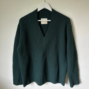 Mörkgrön stickad tröja A Day's March - Snygg mörkgrön stickad tröja från A Day's March i 100% lammull. Modellen har djup v-ringning, ribbad struktur och långa ärmar. Perfekt för dig som gillar klassisk stil med en modern touch. Passar dig som vill ha en varm och mjuk tröja under kyliga dagar. 1E5