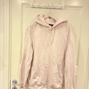 Ljusrosa hoodie från H&M - En ljusrosa hoodie från H&M med huva och snörning. Tröjan har en klassisk känguruficka framtill och långa ärmar. Perfekt för en chill och avslappnad stil. Tillverkad i mjuk bomullsmix som känns skön mot huden.