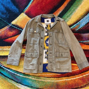 Unik Vintage Daughters of the Liberation feildjacket perfekt skick   - Snygg feildjacket i militärgrönt från Daughters of the Liberation. Jackan har fyra fickor framtill och cool stickad rygg i vitt, blått och gult med grafiskt mönster. Perfekt statement-plagg för dig som vill sticka ut. I storlek Xs men passar som M väldigt svår att hitta riktigt sällsynt DM för fler bilder eller frågor 🇯🇲🌵🦥