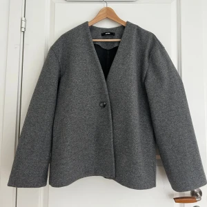Grå kappa från BikBok - Stilren grå kappa från BikBok i med rak passform och v-ringad hals. Jackan har en enkel knäppning framtill med en knapp och långa ärmar. Den är större i storlek så är mer som M än S. 