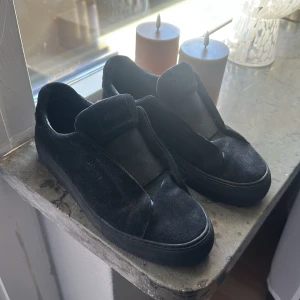 Svarta sneakers från Axel Arigato - Stilrena svarta sneakers från Axel Arigato i mocka och skinn. Modellen har bred resår över vristen istället för klassisk snörning, vilket ger en clean och modern look. Platt sula och rund tå gör dem både snygga och bekväma till vardags. (Kvitto och Box ingår)