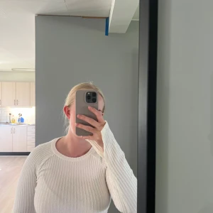 Vit ribbad långärmad croptop - Säljer en vit ribbad långärmad croptop med rund halsringning. Tröjan är figurnära och har stretchigt material. Har slits vid ärmarna 