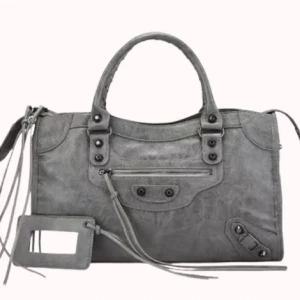 Grå handväska i skinn med detaljer - Snygg grå handväska i skinn med coola metalldetaljer, dragkedja framtill och långa dekorativa remmar. Väskan har dubbla handtag och en avtagbar spegel. Perfekt för dig som gillar en edgy och stilren look.