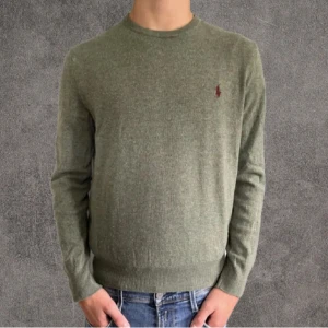 Olivgrön merinoull tröja Polo Ralph Lauren - Snygg olivgrön stickad tröja från Polo Ralph Lauren med klassisk rund hals och broderad vinröd logga på bröstet. Tröjan har ribbade muddar och är långärmad, perfekt för lager-på-lager under höst och vinter. Små små hål som inte syns vid användning Står storlek M men sitter som S-XS skulle jag säga 