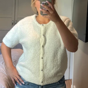 Vit fluffig kofta med pärlknappar - Supermjuk och fluffig vit kofta från Bik Bok med kort ärm och rund hals. Snygga pärlknappar framtill ger en extra touch. Perfekt att slänga på sig över ett linne eller t-shirt. Materialet känns riktigt gosigt och passar året runt. Aldrig använt 