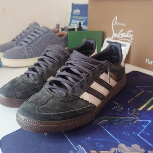 Adidas Spezial sneakers i mörkgrön mocka - Snygga Adidas Spezial sneakers i mörkgrön mocka med klassiska vita ränder och gummisula. Skorna har guldfärgad Spezial-logga på sidan, svarta detaljer och grå snörning. Perfekta för dig som gillar retrostil och streetwear.