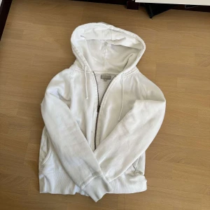 Vit hoodie från Northbrook Sports - Säljer en vit zip up hoodie från Northbrook Sports i storlek 38. Tröjan har huva med snörning, dragkedja framtill och två fickor. Den är croppad i modellen och har långa ärmar. Materialet är mjukt och känns som bomull, perfekt för chill dagar 💓. 