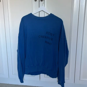 Blå sweatshirt från Pull&Bear M - Blå oversized sweatshirt från Pull&Bear med trycket 'EDGY CREATIVE MIND' på bröstet. Tröjan har rund hals, långa ärmar och är gjord i mjuk bomull. Perfekt för en chill och avslappnad stil.