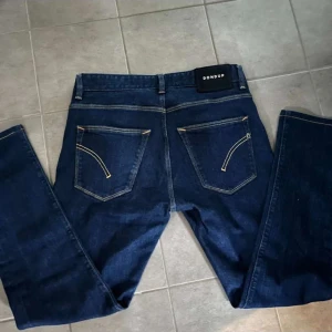 Dondup Jeans - Snygga blå jeans från Dondup med klassisk femficksdesign och kontrastsömmar. Jeansen har raka ben och normal passform, tillverkade i slitstarkt bomullsjeans. Bakfickorna har en unik gulddetalj som sticker ut. Perfekta för dig som gillar stilrena och italienska jeans. Storleks taggarna är av samt med tvätt måtten.