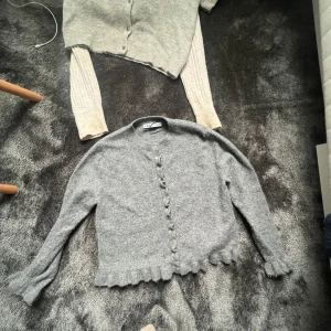 Grå kofta med volangkant  - Superfin grå kofta från Zara  med volangkant nertill och längs ärmsluten. Koftan har rund halsringning, knappar framtill och är stickad i mjukt material. Perfekt att slänga över en topp för en chill look.  SKRIV FÖR FLER BILDER 