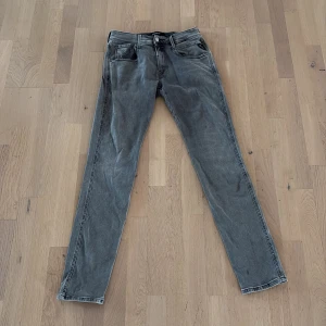 Replay Hyperflex grå jeans - Snygga grå Replay Hyperflex jeans med klassisk femficksdesign och raka ben. Jeansen har en diskret tvättad look, svarta detaljer och stretchigt material som gör dem riktigt sköna. Perfekta för dig som gillar en stilren och avslappnad vibe.