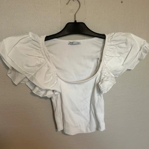 Vit volangtopp från Zara - Superfin topp med volangärmar från zara, den är aldrig använd har dock dragit av lapparna. Jättefin till festliga tillfällen!