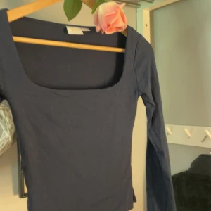 Mörkblå långärmad topp Gina Tricot - Snygg mörkblå långärmad topp från Gina Tricot i storlek XS. Modellen har en djup fyrkantig urringning och är figurnära. Perfekt att styla med jeans eller kjol för en clean look. Materialet känns mjukt och stretchigt, troligen bomull med lite syntet.