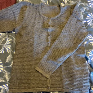 Grå kofta med struktur och knappar - Mysig grå kofta med snyggt strukturerat mönster och rund halsringning. Knappar framtill och långa ärmar. Perfekt för lager-på-lager och chill dagar. Passar dig som gillar enkel men stilren look.