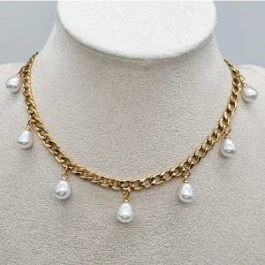 Guldhalsband med droppformade pärlor - Stilrent halsband i guldtonad kedja med sju droppformade vita pärlor som hänger längs länkarna. Perfekt statement piece för dig som vill sticka ut med en elegant och trendig accessoar. Kedjan har en klassisk design och pärlorna ger en lyxig vibe.