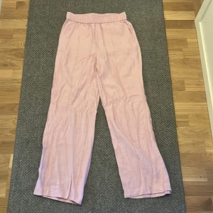 Ljusrosa linnebyxor från H&M - Säljer ett par ljusrosa linnebyxor från H&M i storlek S. Byxorna har elastisk midja och raka, lite bredare ben för en chill och skön vibe. Perfekta för varma dagar och riktigt snygga till sneakers eller sandaler.