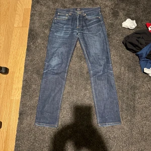 A.P.C. Petit Standard jeans blå 28 - Snygga blå jeans från A.P.C. Petit Standard i klassisk straight fit. Modellen har fem fickor, orange kontrastsömmar och knappgylf. Jeansen är tillverkade i slitstarkt bomullsdenim och har en mörkblå tvätt med lätt faded effekt. Perfekt för dig som gillar minimalistisk stil.