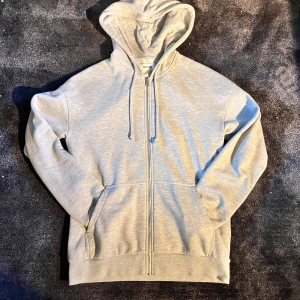 Grå hoodie med dragkedja och huva - XS men passar som en S. Snygg grå hoodie från Polaris med hel dragkedja framtill, huva med snörning och två praktiska fickor. Mjuk bomullsmix som är skön att ha på sig och passar perfekt till jeans eller joggers. Klassisk modell med lång ärm och ribbade muddar.