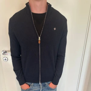 Mörkblå kofta med dragkedja från Morris - Snygg mörkblå kofta från Morris med hel dragkedja och liten broderad logga på bröstet. Tröjan har lång ärm, ribbade muddar och står upp lite i kragen. Perfekt till jeans och funkar året runt. Använd 2-3 ggr, nästan helt ny. Modell 176, väger 65. Storlek M men passar även S