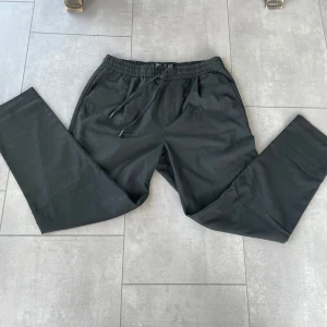 Svarta byxor Pull&Bear M - Svarta mjukisbyxor från Pull&Bear i storlek M. Byxorna har elastisk midja med snörning, raka ben och fickor både fram och bak. Perfekta för en chill och avslappnad stil. Materialet känns mjukt och bekvämt.