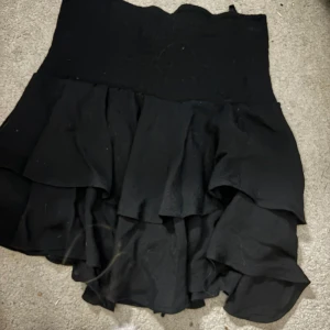 Svart volangkjol med hög midja - Supersnygg svart kortkjol med flera lager volanger och hög midja. Kjolen har en flowy känsla och passar perfekt till en trendig outfit. Enkel att matcha med både crop tops och stickade tröjor.