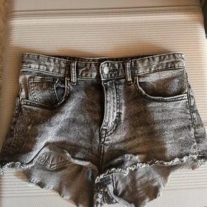 Grå jeansshorts med rå kant H&M - Snygga grå jeansshorts från H&M i tvättad denim med råa, fransiga kanter. Klassisk femficksmodell och knappgylf. Perfekta för sommardagar när du vill ha en avslappnad och cool stil.