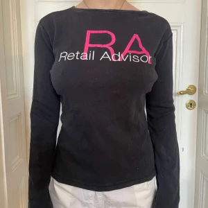 Svart långärmad tröja River Island - Svart långärmad tröja från River Island med tryck 'Retail Advisor' i vitt och rosa framtill och logga på ryggen. Tröjan har en enkel, rak passform och är gjord i mjuk bomull. Perfekt för dig som gillar stilrena basplagg med en twist. Den är faktiskt bak och fram här, men jag tyckte det var fint😌