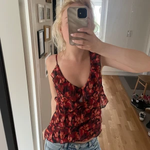 Röd volangtop - Boohoo - Säljer en snygg röd och svart linnetopp från Boohoo med volangdetaljer och smala axelband. Toppen har ett abstrakt mönster och djup v-ringning, säljs inte längre heller. Lätt och luftig känsla, passar till jeans eller kjol.💕☺️använd en gång 