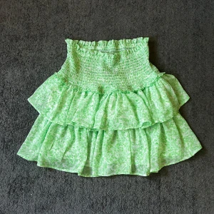 Grön volangkjol från ONLY - Supersöt grön kortkjol från ONLY med blommigt mönster och volanger. Kjolen har smock i midjan för en bekväm passform och är gjord i ett lätt, flowy material. Använd ett fåtal gånger och säljer den då den är lite för stor för mig💚🌸