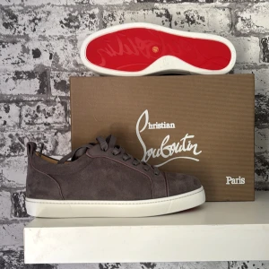 Grå mockasneakers från Christian Louboutin - Snygga grå sneakers i mocka från Christian Louboutin med klassisk vit sula och ikonisk röd undersida. Skorna har rund tå, platt sula och grå snörning. Perfekta för dig som vill ha en lyxig och stilren look med en touch av Paris.
