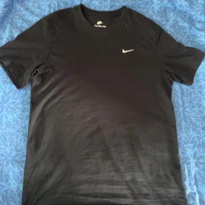 Svart Nike t-shirt i bomull - En stilren svart t-shirt från Nike med klassisk rund hals och diskret Nike Swoosh-logga på bröstet. Tillverkad i mjuk bomull som är skön att bära. Perfekt för en clean och sportig look.