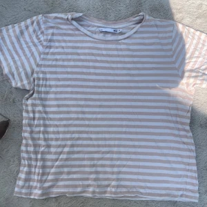 Randig t-shirt från 157, beige/vit - Säljer en kortärmad t-shirt från 157 i storlek M. T-shirten har beige och vita horisontella ränder och är gjord i mjuk bomull. Klassisk rund halsringning och relaxed fit, perfekt till jeans eller shorts.