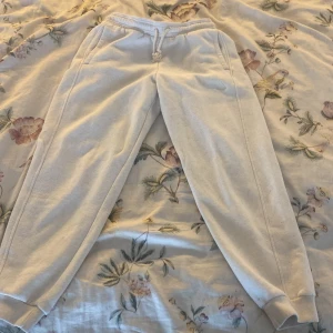 Beige mjukisbyxor från Adidas - Säljer ett par beige mjukisbyxor från Adidas med broderad logga på ena benet. Byxorna har resår och snörning i midjan samt muddar vid bensluten. Perfekta för chill eller träning, tillverkade i mjuk bomullsmix.