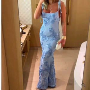 Ljusblå långklänning med blommor - Aldrig använd supersnygg ljusblå långklänning med tunna axelband som knyts på axlarna. Klänningen har broderade blommor i blått och sitter figurnära. Klänningen är från Majive ord pris 469kr. Första bilden är från Majives hemsida, klänningen är lång så därför fick inte hela plats i bilderna. Kontakta mig om du vill ha fler bilder mm.