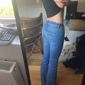 Blå jeans från Vero Moda - Snygga blå bootcut jeans från Vero Moda med låg midja. Jeansen har klassisk femficksdesign, dragkedja och knapp framtill. Passar mig som har 24/32 i jeans! Har lite slitningar nere vid hälarna och på vänstra låret, därav priset!