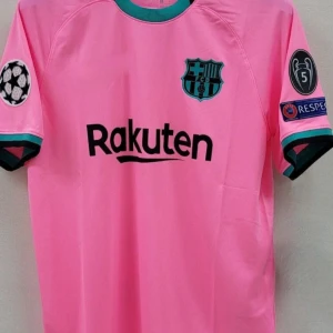 Rosa FC Barcelona fotbollströja - Snygg rosa FC Barcelona fotbollströja med svarta och turkosa detaljer. Kortärmad modell med klubbmärke på bröstet, Rakuten-logga och Champions League-patchar på armen. 
