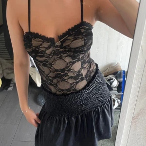 Svart spetsbody med tunna axelband - Säljer en snygg spetsbody med transparent spets och tunna axelband. Toppen har en markerad byst, dekorativ spetskant upptill och figurnära passform. Perfekt för dig som vill ha en edgy och trendig look.
