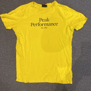 Gul Peak Performance t-shirt - Snygg gul t-shirt från Peak Performance med svart tryck på bröstet. Klassisk rund hals och korta ärmar. 